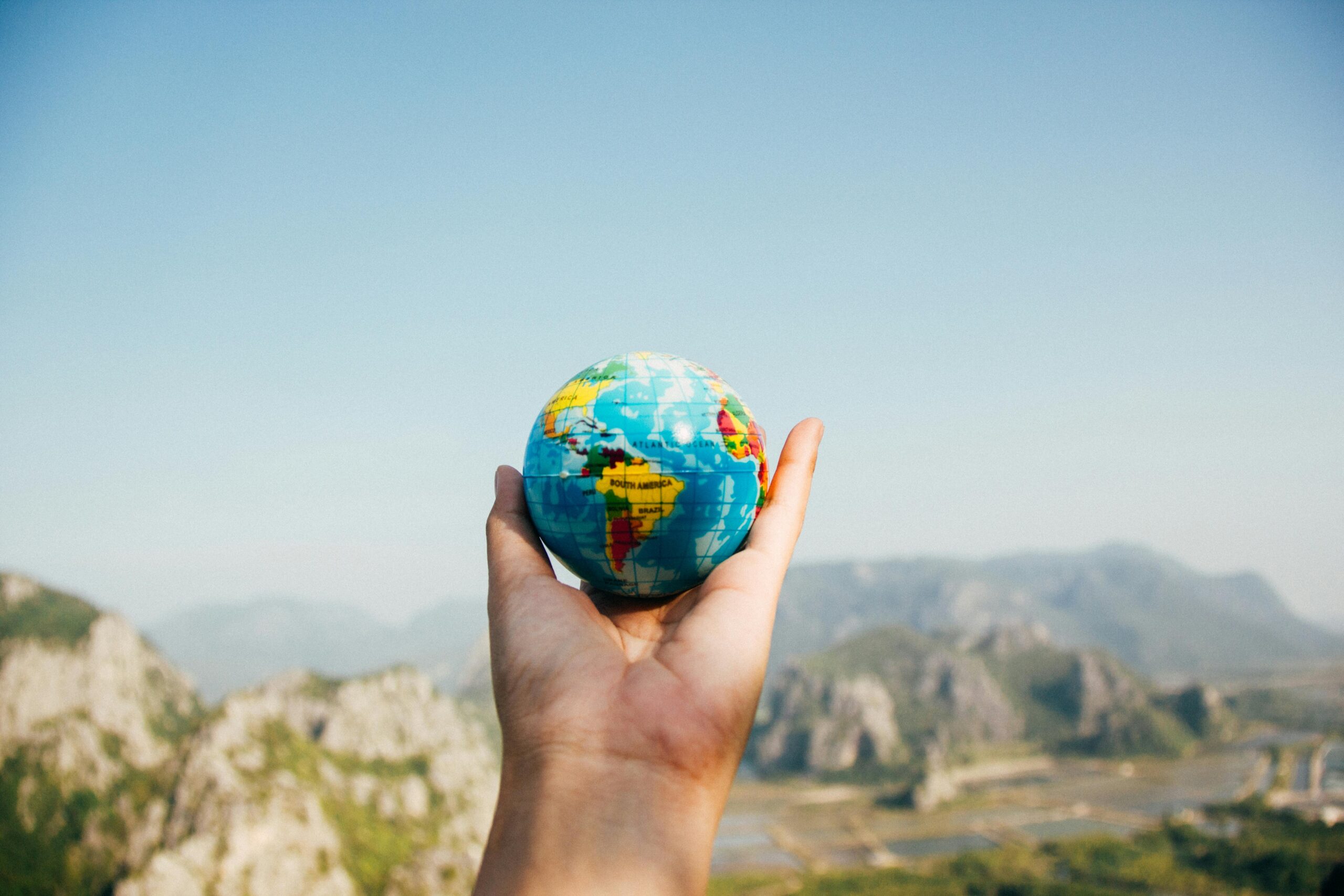 Hand holding a globe in front of a mountain landscape, emphasizing the globalized nature of the international school approach.